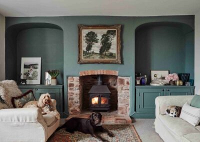 A green-walled sitting room with a lit fireplace and dogs resting on the sofas at the Country Dog Hotel