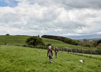 Two handlers walking a dog across the rolling Somerset hillside with far-reaching countryside views