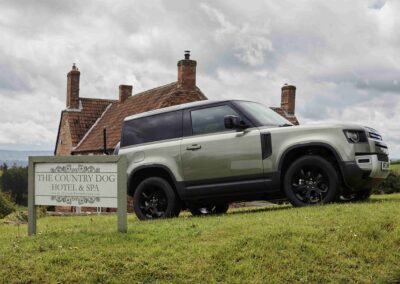 A Land Rover Defender parked beside the wooden Country Dog Hotel & Spa sign, with the Somerset farmhouse behind